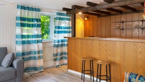 A kitchen with wooden cabinets, a bar area, and a window with curtains.