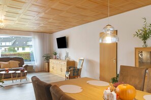 Un salon comprenant un canapé, une table à manger, des chaises, un téléviseur et une grande fenêtre.