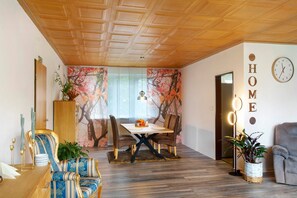 Un coin repas avec un plafond en bois, une table avec des chaises, une horloge murale et une enseigne indiquant « MAISON ».
