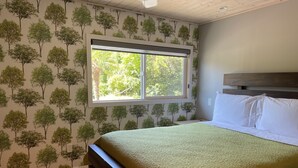 A bedroom with a bed, a window, and a wall with a tree pattern. - Two Cottages on Waterfront Property with Beach Access - Sleeps 10 (Sooke)