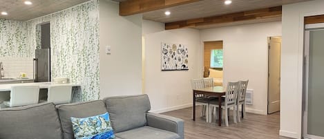 A modern living room with a grey sofa, a blue ottoman, and a dining area with a wooden table and chairs.