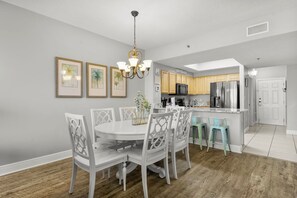 A modern kitchen with white cabinetry, a central island, and a dining area with white chairs and a chandelier. - Ariel Dunes I 1803 *Stunning Beach Views*Pools* (Miramar Beach)