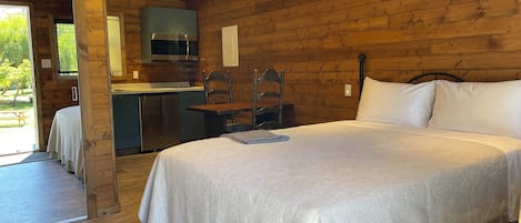 A wooden cabin with a bed, a dining table, and a kitchenette.