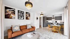 A modern living room with a brown sofa, a round coffee table, and a dining area with yellow chairs. - Brandnew Luxurious 2bedApartment (Ebbsfleet Valley)