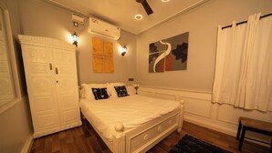 A bedroom with a white bed, a wooden floor, a black rug, a white wardrobe, and a painting on the wall. - Eden Garden By Jolly Homes (Madurai)