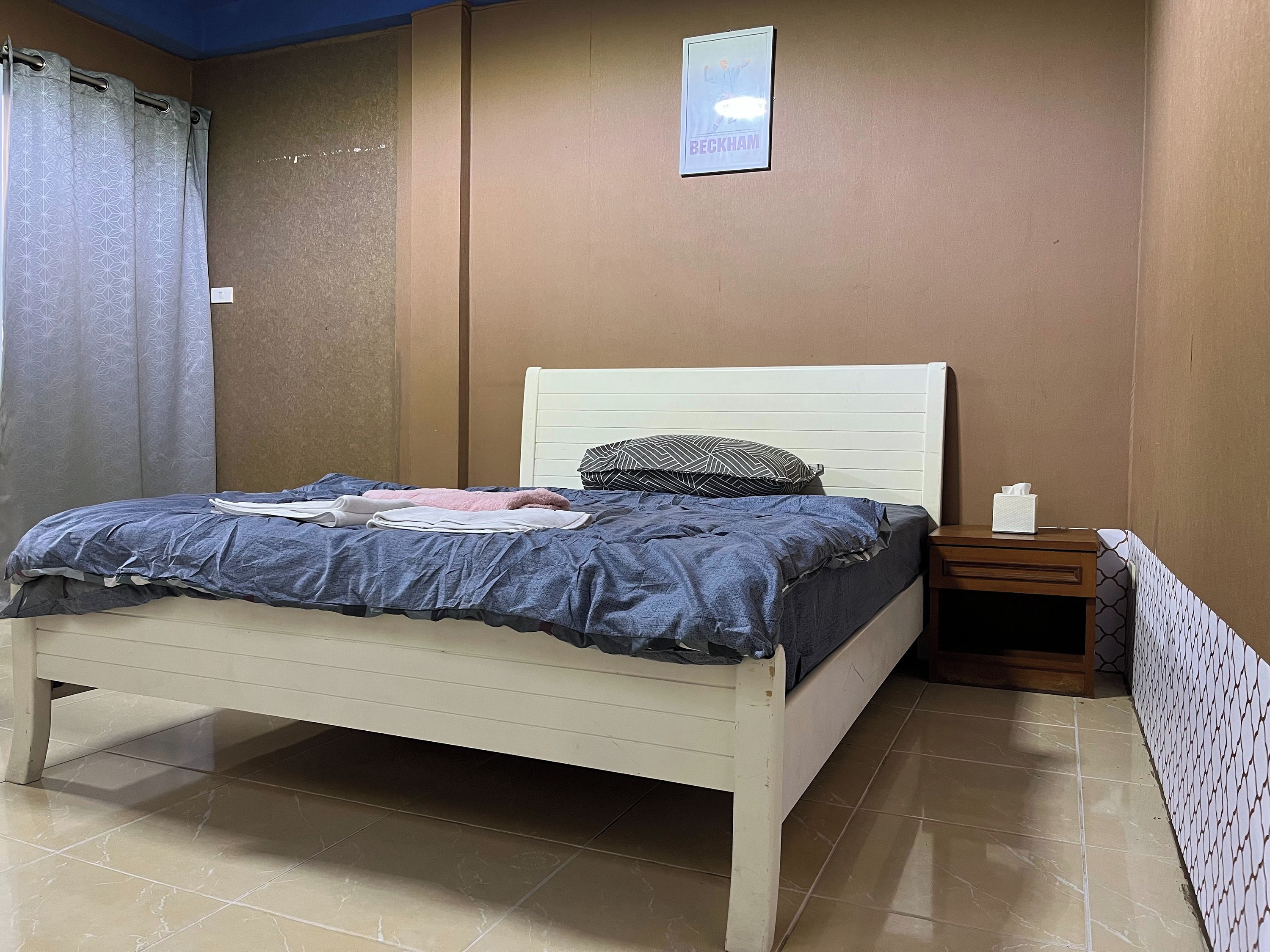 A neatly made bed with a white headboard, a bedside table with a tissue box, and a framed picture on the wall.