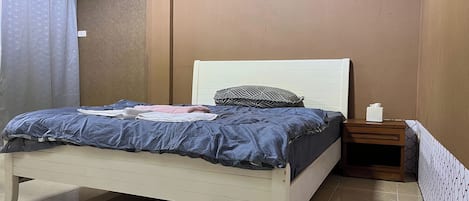 A neatly made bed with a white headboard, a bedside table with a tissue box, and a framed picture on the wall.