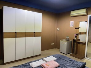 A hotel room with a bed, a wardrobe, a small refrigerator, and an air conditioning unit.