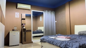A bedroom with a bed, a wardrobe, a small refrigerator, and an air conditioning unit.