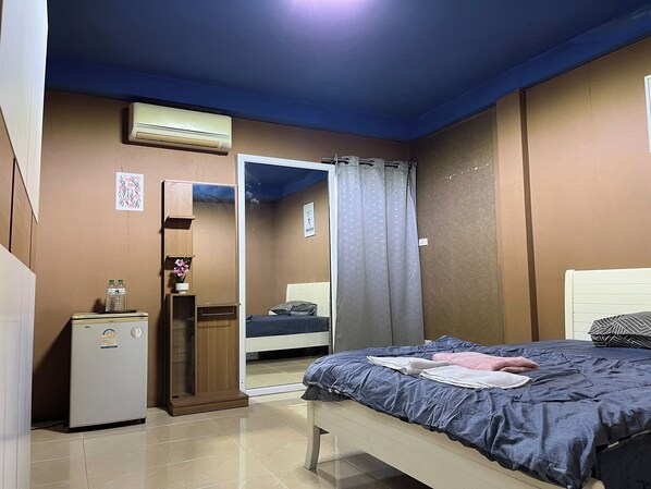 A bedroom with a bed, a wardrobe, a small refrigerator, and an air conditioning unit.