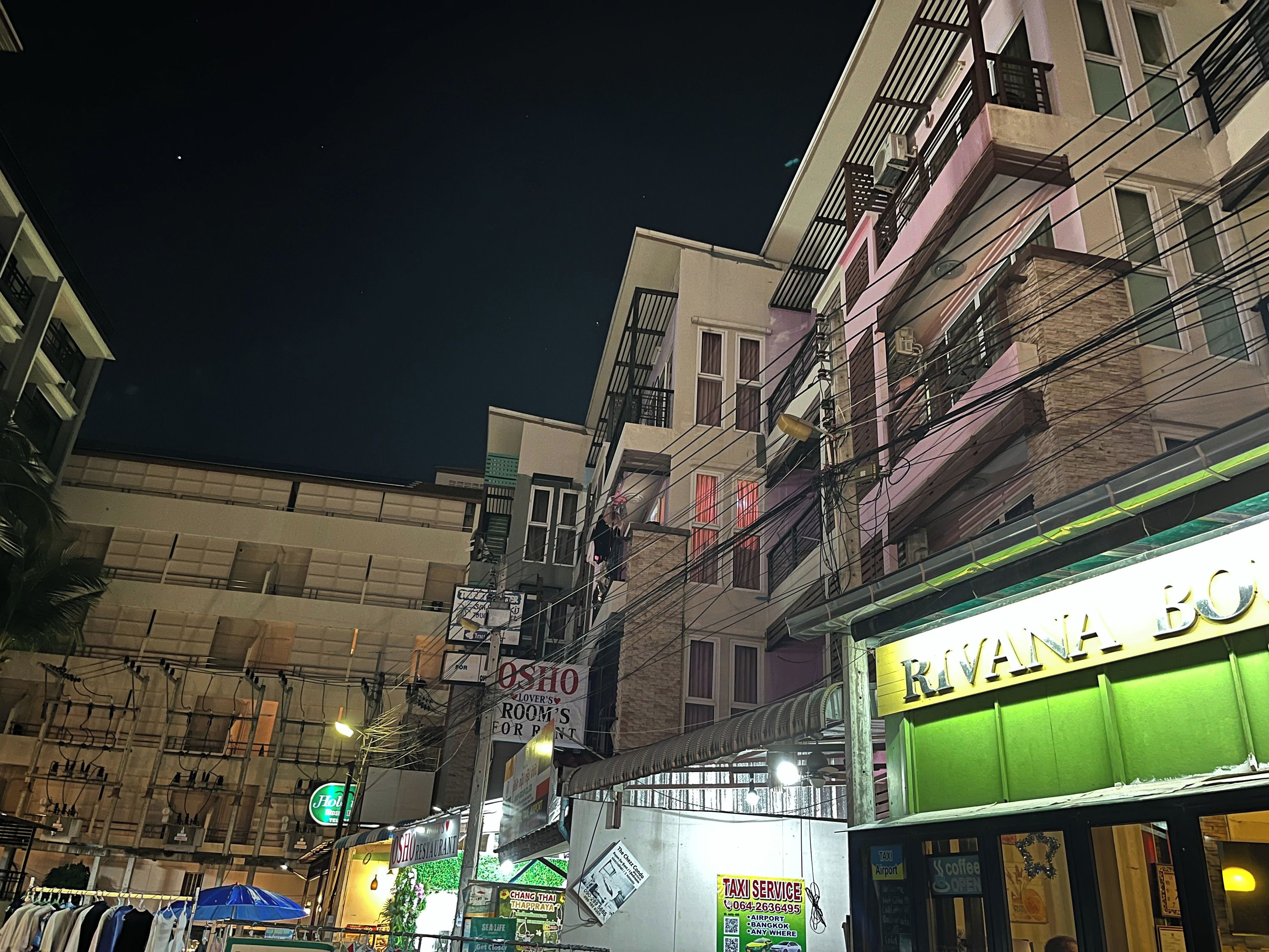 A street view at night with buildings, a sign for 'Rivana Bo' restaurant, and a 'Taxi Service' sign.