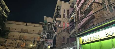 Vista nocturna de una calle con edificios, un cartel del restaurante 'Rivana Bo' y un letrero de 'Taxi Service'.