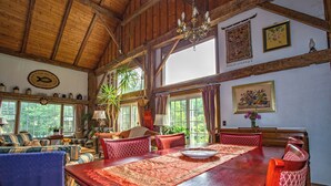 A spacious room with a wooden ceiling, a dining table with red and gold tablecloths, and a large window with curtains. - Charming Barn Home Near Jiminy Peak (Hancock)