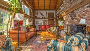 A cozy, rustic living room with wooden beams, a brick fireplace, and comfortable seating. - Charming Barn Home Near Jiminy Peak (Hancock)