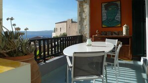 A balcony with a round table and chairs, a potted plant, and a view of the sea.