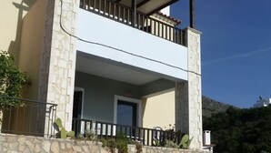 A two-story house with a stone facade, a balcony, and a car parked in front.