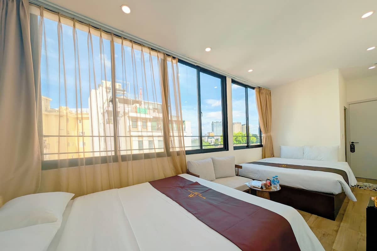 A hotel room with two beds, a large window with curtains, and a view of buildings outside.