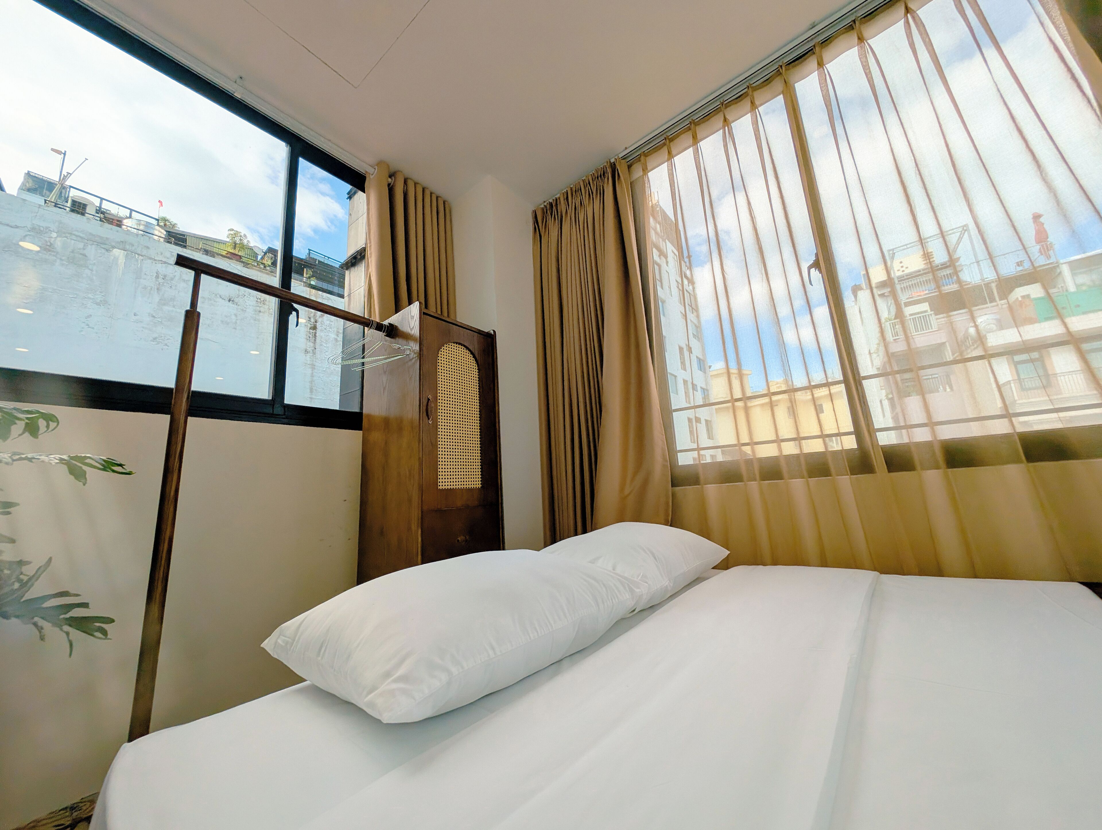 Een hotelkamer met een bed, een raam met gordijnen en uitzicht op gebouwen.