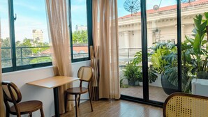 Un balcon avec une table et des chaises, de grandes fenêtres avec des rideaux et des plantes en pot.