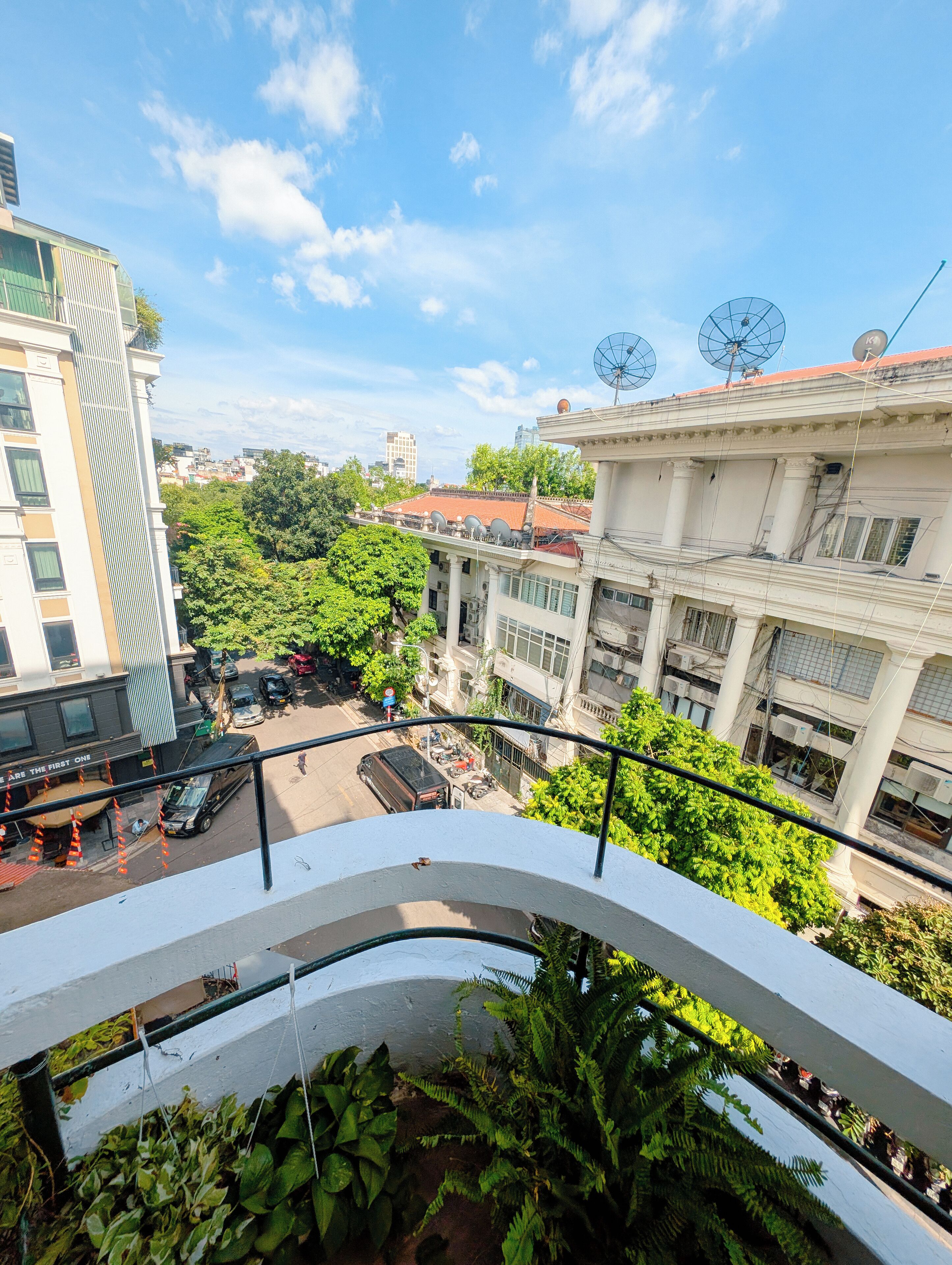 A view from a balcony overlooking a cityscape with buildings, greenery, and a clear sky.