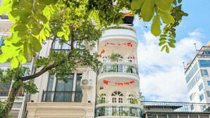 Un immeuble à plusieurs étages doté de balcons, avec un restaurant appelé « Maison Maravelle » au rez-de-chaussée et divers commerces au niveau du sol.