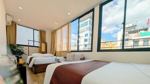 Une chambre d’hôtel avec deux lits, un bureau, une plante et de grandes fenêtres donnant sur la ville.