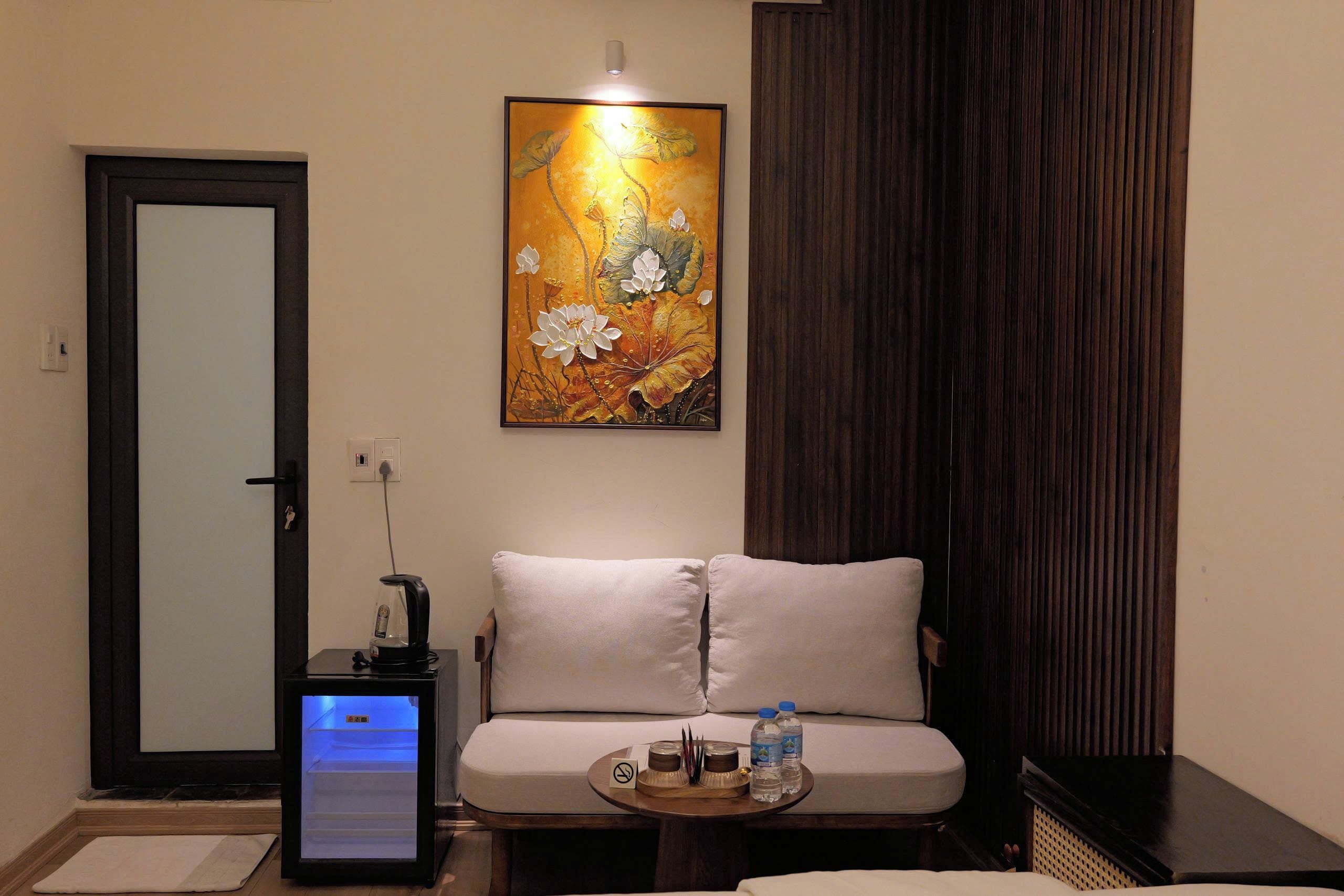 A hotel room with a sofa, a small table with water bottles, a coffee machine, and a painting on the wall.