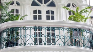 Un bâtiment blanc doté de fenêtres en arc de cercle et d’un balcon orné de balustrades en fer forgé vert.