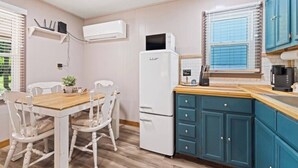 A compact kitchen with a white refrigerator, a microwave, and a coffee maker on the counter. There is a dining table with chairs and a small potted plant on it.