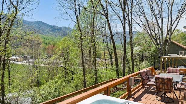 A deck with a hot tub, outdoor furniture, and a view of a mountainous landscape.