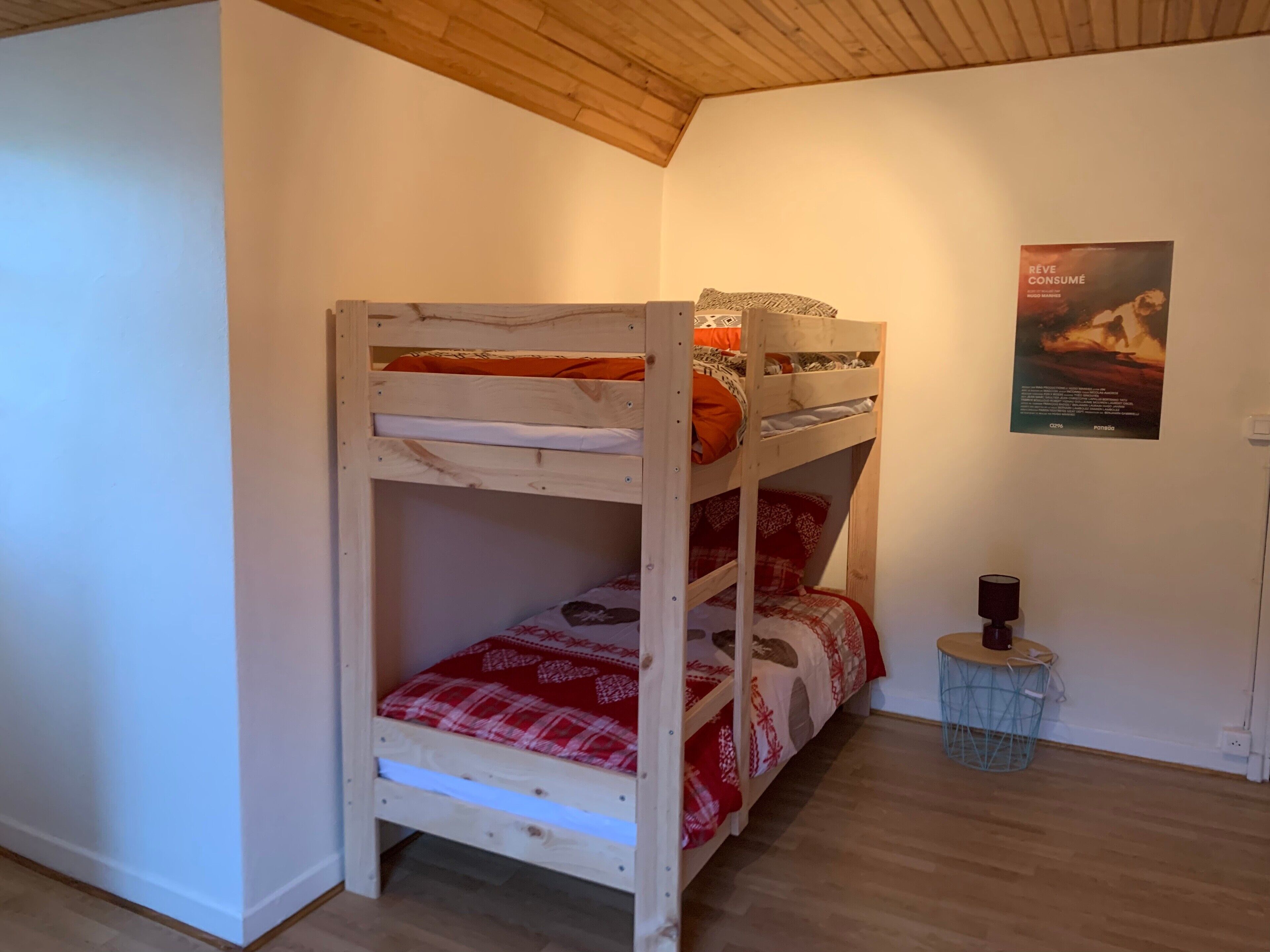 Een stapelbed met een rood-wit geruit laken, een houten plafond en een poster aan de muur.