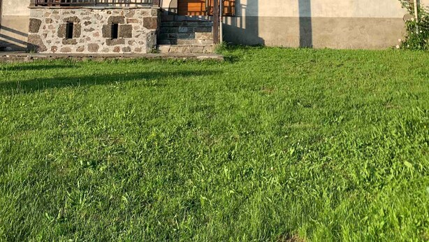 Una casa a due piani con facciata in pietra, un portico in legno e un tetto spiovente.