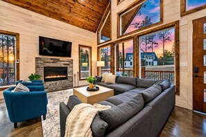 A spacious living room with a stone fireplace, a large sectional sofa, and a television mounted on the wall.