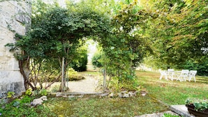 A garden with a stone pathway, white outdoor furniture, and a pergola covered with climbing plants.