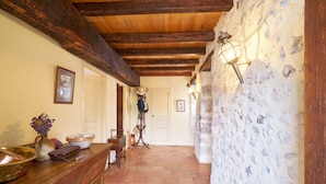 A hallway with a wooden ceiling, a stone wall, a wooden counter with various items, and a door at the end.