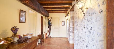 A hallway with a wooden ceiling, a stone wall, a wooden counter with various items, and a door at the end.