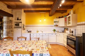 Una cocina con armarios blancos, una estufa y un microondas. Hay dos luces colgantes y un salpicadero de azulejos.