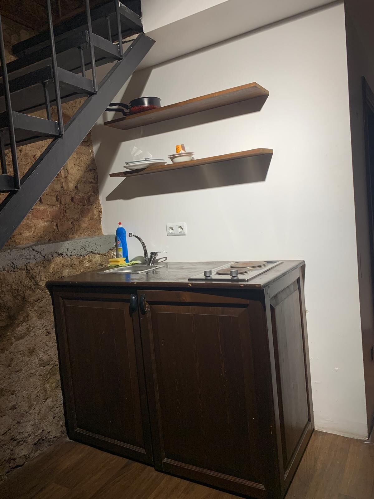 A compact kitchen with a dark wooden cabinet, a built-in stove, and a metal staircase.