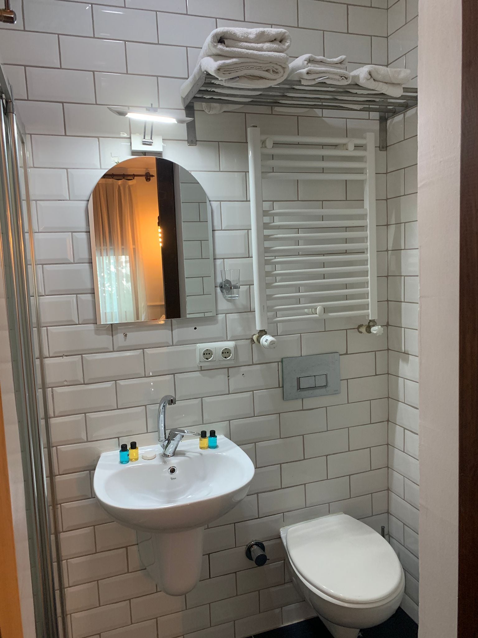 A bathroom with a white sink, mirror, and toilet. There are towels stacked on a rack above the mirror.