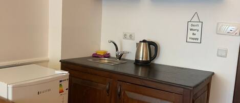 Una cocina compacta con armarios de madera, un refrigerador empotrado y una tetera sobre la encimera.