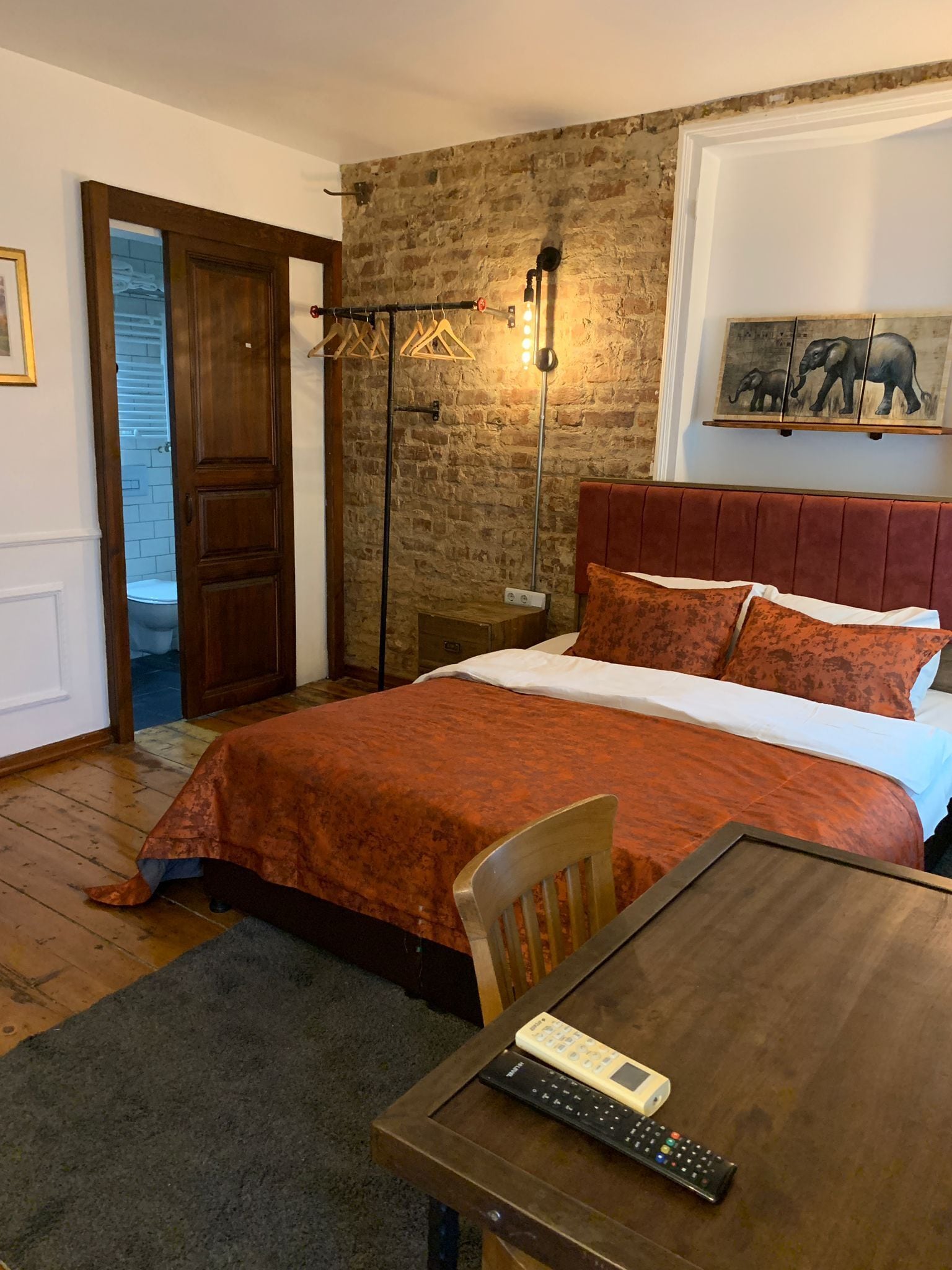 Une chambre à coucher avec un lit en bois, une table de chevet, une lampe et un tableau représentant des éléphants accroché au mur.