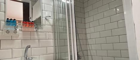 Casa de banho com chuveiro envidraçado, lavatório branco e espelho em cima.