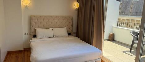 A bedroom with a tufted headboard, a large bed, a sliding glass door to a balcony, and two wall-mounted light fixtures.