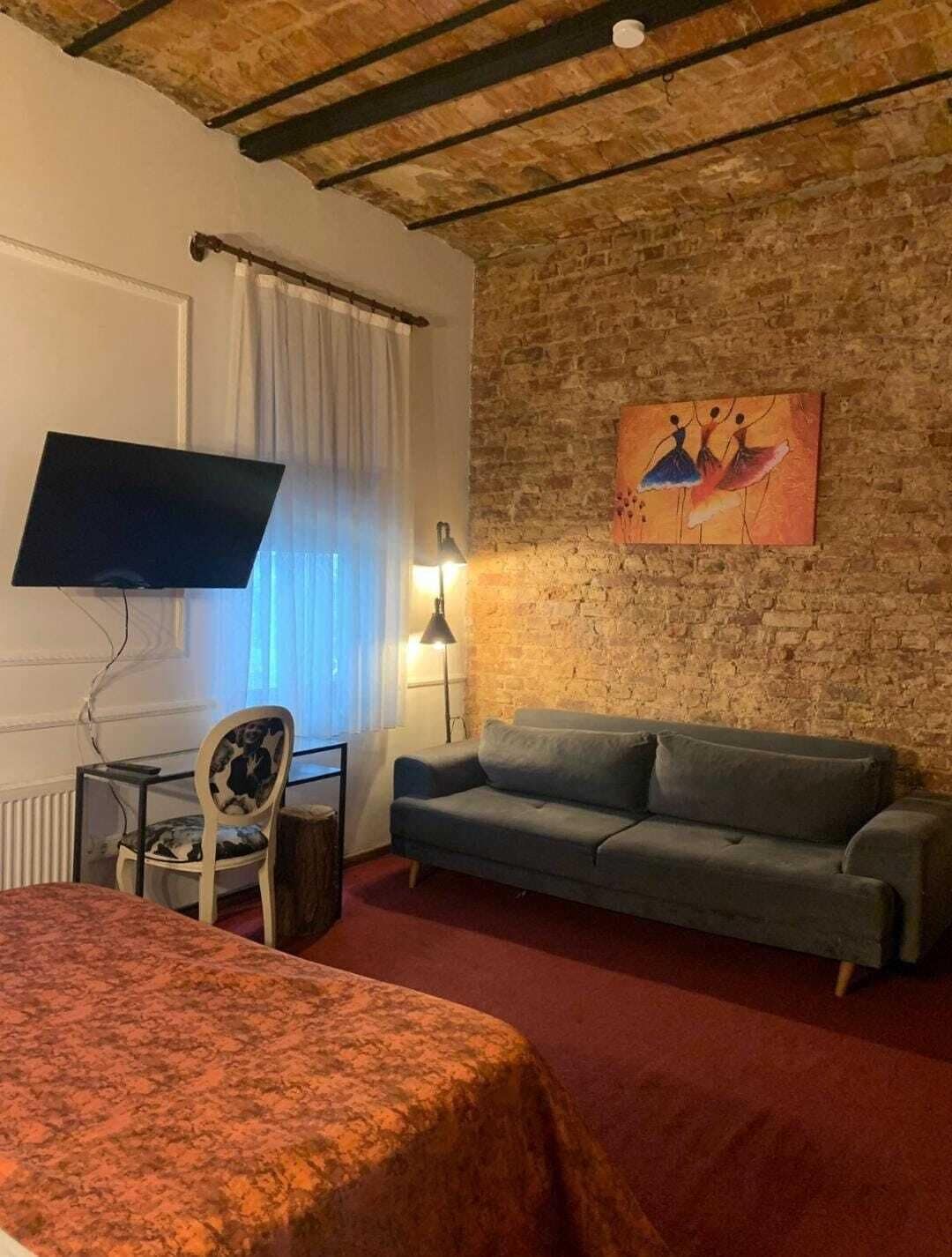 A room with a bed, a sofa, a TV, a lamp, and a painting on a brick wall.
