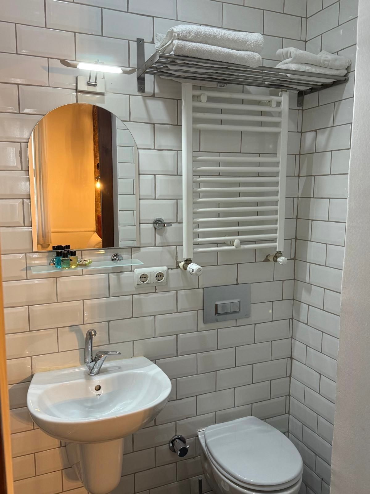 A bathroom with white tiled walls, a white sink, a toilet, a towel rack, and a mirror.
