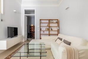 A living room with a TV, sofa, glass coffee table, and a bookshelf.