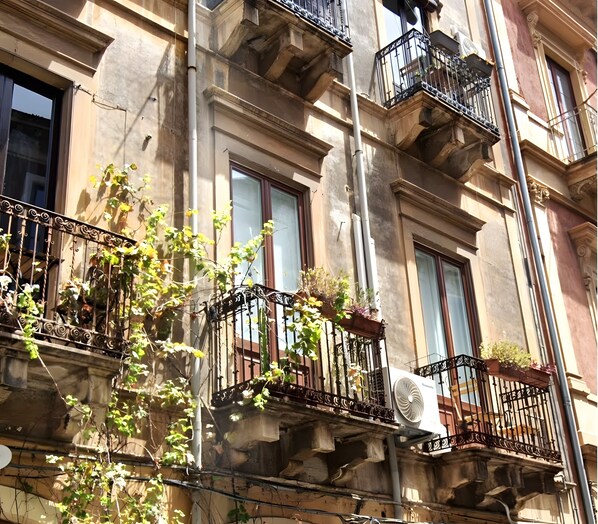 A multi-story building with balconies, some with plants and outdoor furniture.