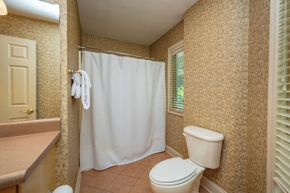 A bathroom with a toilet, shower curtain, and patterned wallpaper.