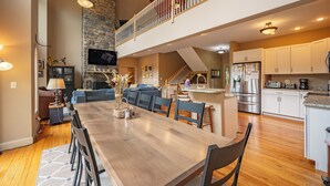 A spacious kitchen with a dining area, a stone fireplace, and a lofted seating area. - Lakefront Luxury Chalet w/ Hot Tub & Dock (McHenry)