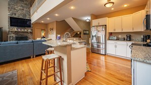 A spacious kitchen with a stone accent wall, a built-in island, and a modern stainless steel refrigerator. - Lakefront Luxury Chalet w/ Hot Tub & Dock (McHenry)